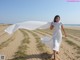 A woman in a white dress walking on a sandy beach.