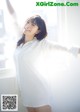 A woman in a white shirt is posing by a window.