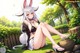 A woman in a bunny costume sitting on a rock in the grass.