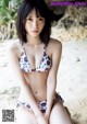 A woman in a bikini sitting on a sandy beach.